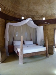 In einer aus Lehmziegeln gebauten Raum mit Kuppel steht ein Himmelbett mit Holzelementen