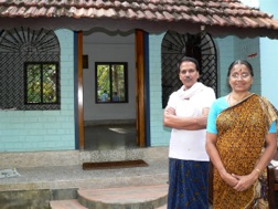 Eine Frau in gelbem Sari und ein Mann mit weißem Hemd stehen vor ihrem Haus